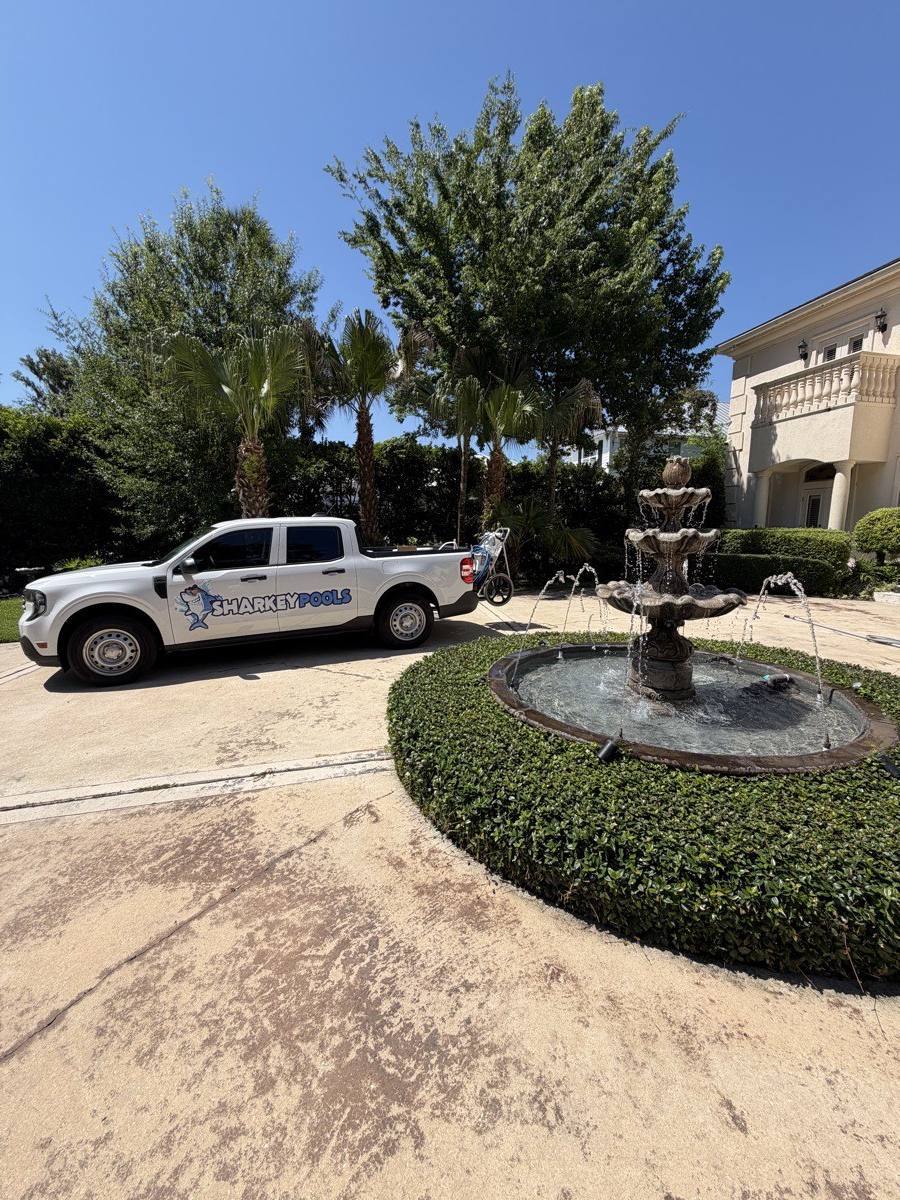 Sharkey Pools truck in the driveway of a large home with a fountain